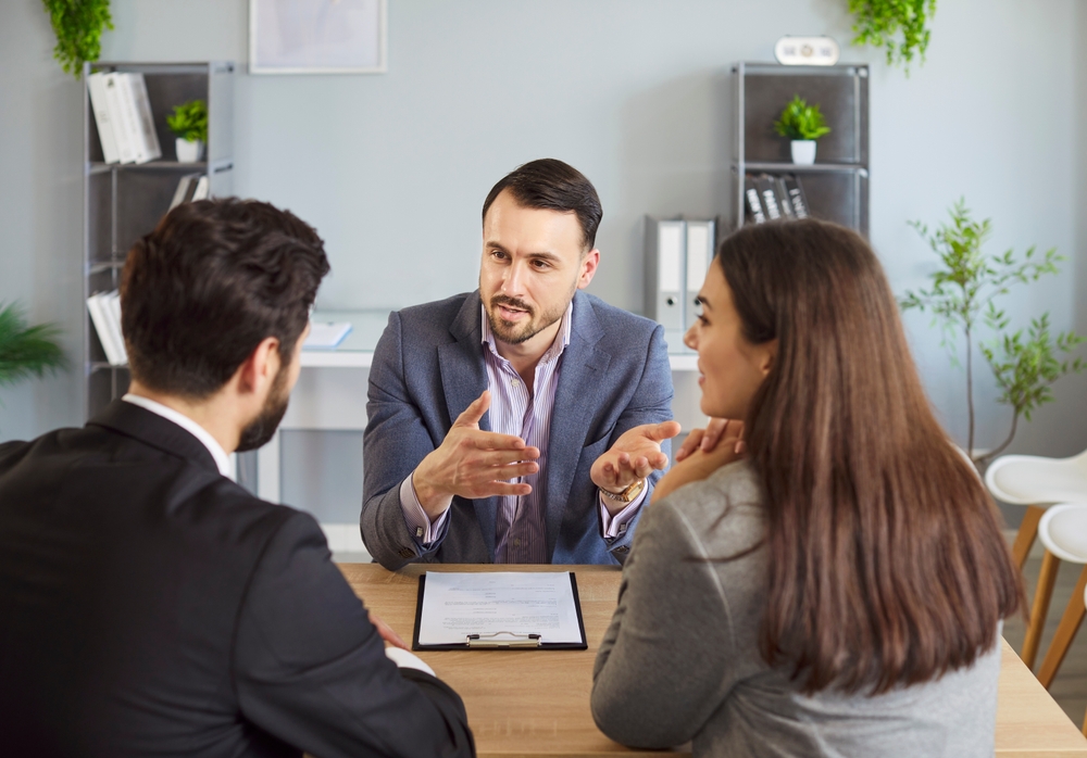 Insurance broker discussing coverage options with two clients during an office meeting.
