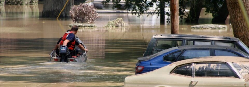 A man sails next to a row of cars in two-foot high flood water after a flood to illustrate water damage.