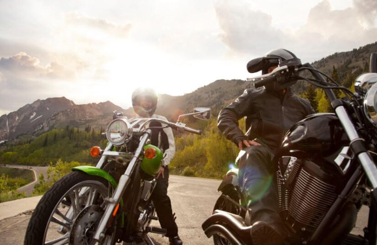Two bikers with motorcycles wearing thick jackets and nice helmets parked on the middle of the road to illustrate the history of motorcycles