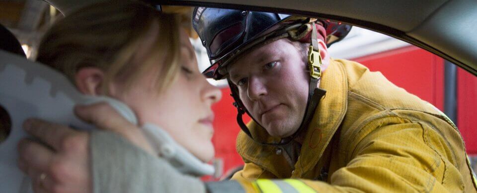A firefighter helping a woman in a neckbrace who was involved in an accident exit a vehicle to illustrate whether pip insurance is right for you
