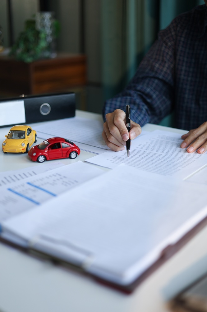 Person signing a car insurance policy with two model cars on the desk.