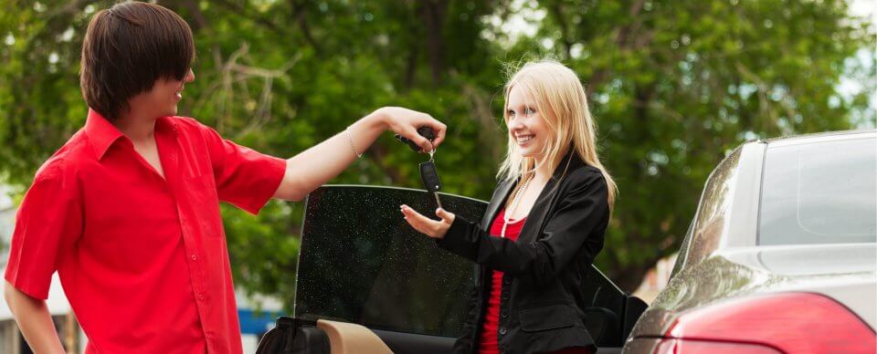 A young Caucasian man handing car keys to a young Caucasian woman to illustrate what happens when a friend borrowed your car and got in an accident.