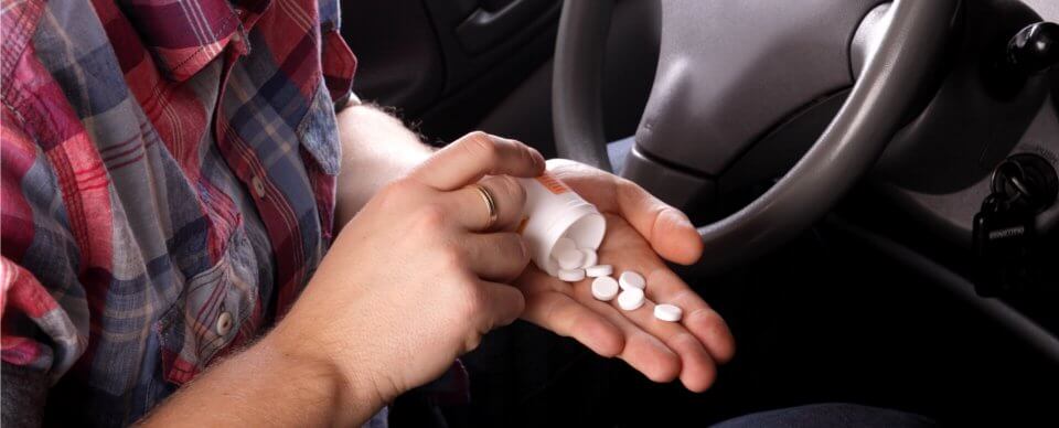 A man holding a handful of pills while sitting at the steering wheel to illustrate how over-the-counter drugs can make you an unsafe driver.