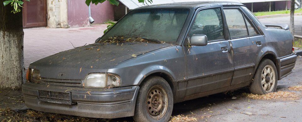 An abandoned car covered in leaves and dirt to illustrate the insurance rates of donating a car to charity.