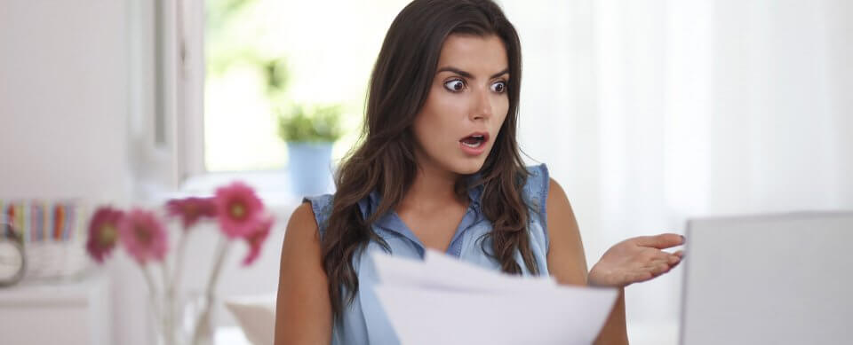 A young, Latino woman looking in awe at her computer because the automatic renewal fees of her auto insurance were unexpected.
