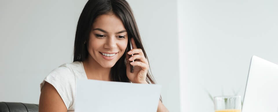 A young latino woman smiling while looking at an insurance policy because she read the tips to lower auto-insurance rates.