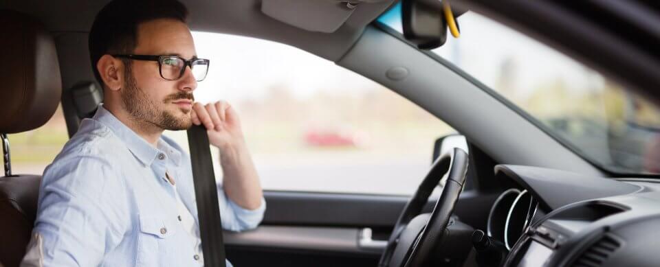 A young, Caucasian man buckling up in his car to illustrate how seatbelts used improperly cause injury.