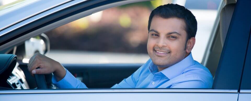 A young, Latino driver sitting on the driver's seat who illustrates ways for immigrants to get cheap auto-insurance.