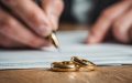 Person signing divorce documents with wedding rings on the table, representing marital status and auto insurance rates.