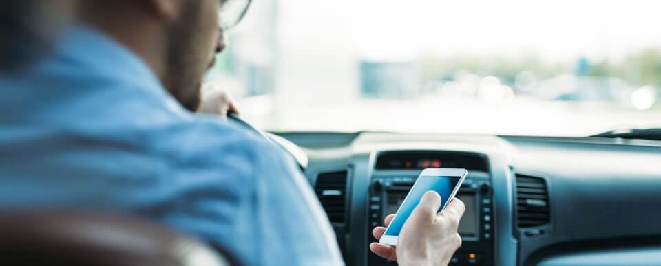 A man texting and driving who illustrates dangerous driving habits that increase the risk of an accident.