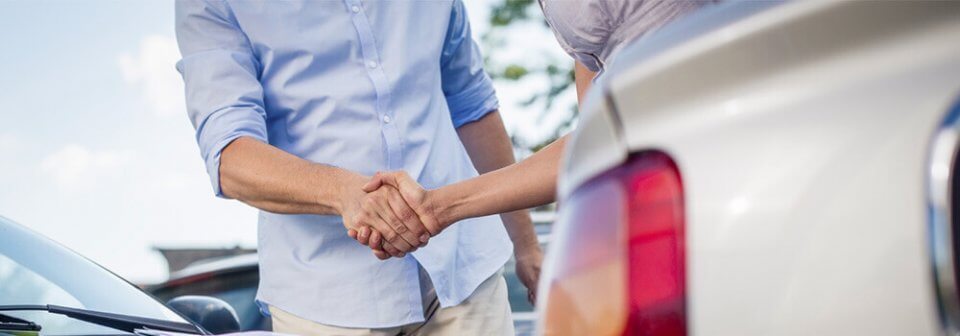 Two men shaking hands next to their vehicles after they were involved in a car accident.