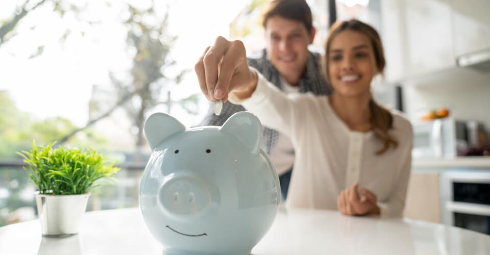 A multi-ethnic couple putting coins in a piggy-bank to portray a way to save your money.