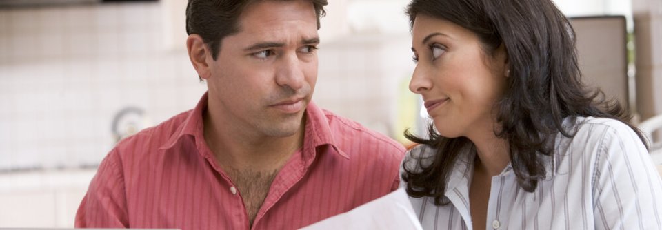 Couple in kitchen with car insurance paperwork looking at each other with worry because their car insurance rates were higher than expected.