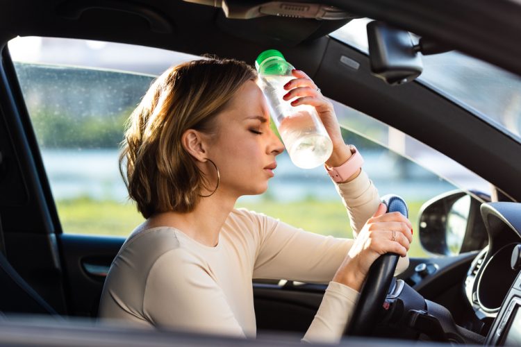 woman behind the wheel presses water bottle to her head to relieve heat