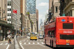 Busy New York City street with cars, taxis, and a sightseeing bus, illustrating everyday driving and car insurance needs in New York.