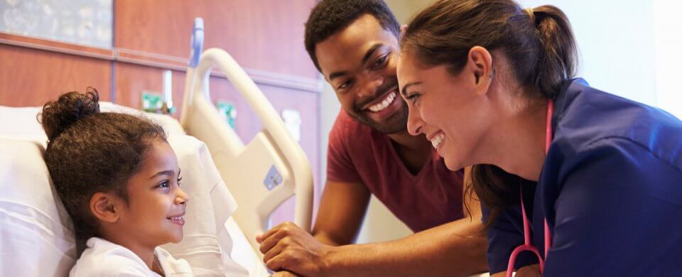 A young multi-ethnic family looking at its daughter, who lies in a hospital bed and illustrates why healthcare for children is so important.