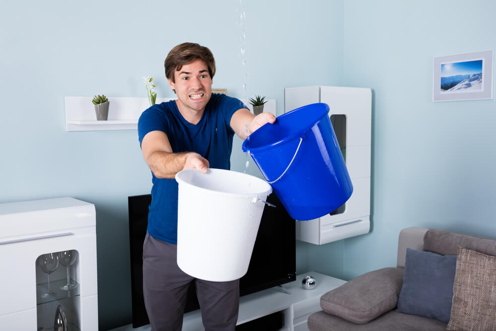 man in apartment gathering water from leak with two buckets 