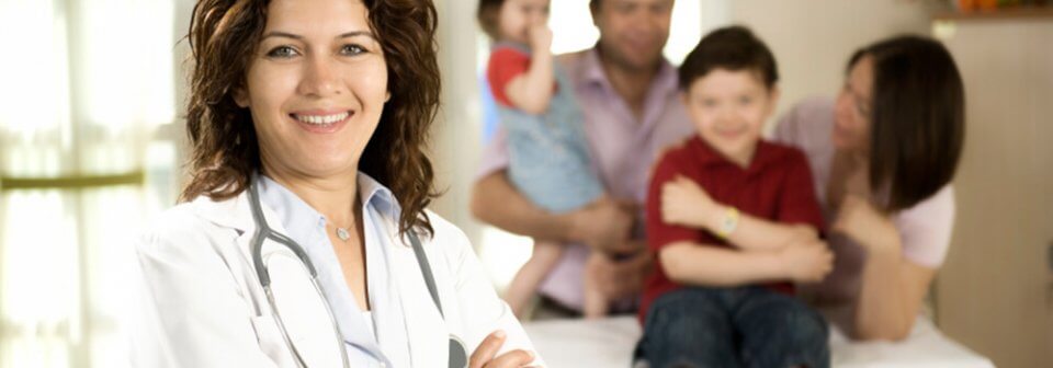 Female doctor smiling arms crossed while young patient is in the background with parents to illustrate how to pick the right health insurance plan.