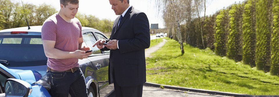 An insurance adjuster talking to a man who was just involved in a major accident and illustrating how to file a car insurance claim.