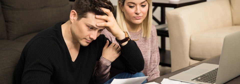 Young couple looking stressed and overwhelmed in front of a bunch of unpaid bills because they left their auto-insurance lapse.