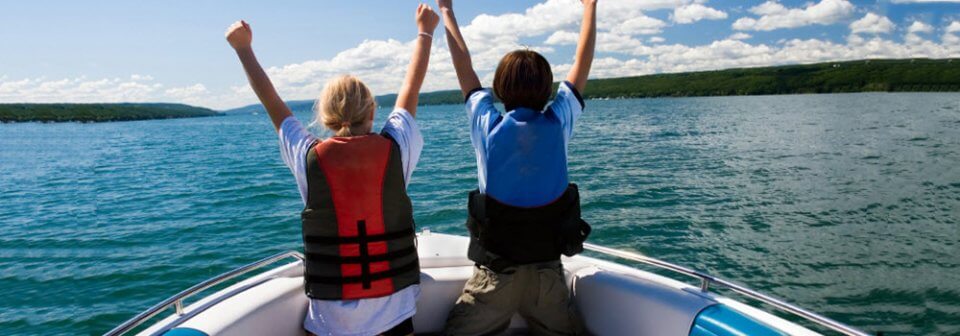Two young kids wearing life vests while sailing to illustrate the requirements for personal watercraft and the importance of insurance.
