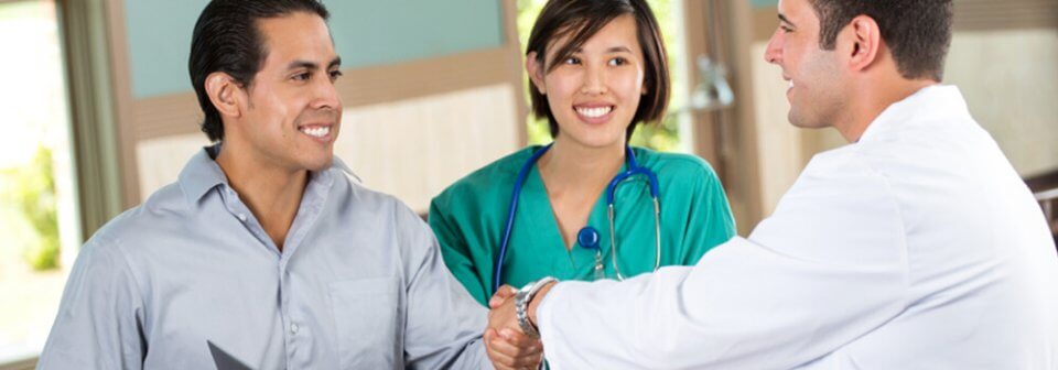 Smiling Hispanic man shaking doctors hand in hospital and illustrating what is the difference between MediCal and Medicaid.