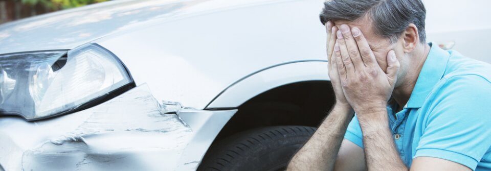 A middle-age man covering his face in desperation after Someone Dented His Car and damaged his bumper.