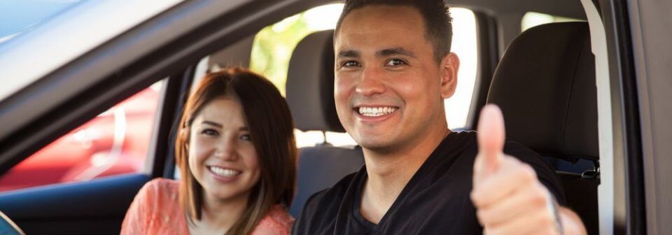 Happy latino couple sitting in car and smiling because he found cheap car insurance depict 10 ways to get cheap car insurance.