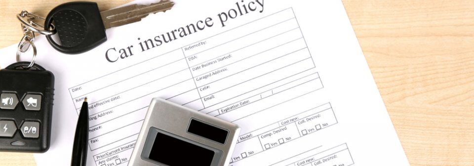 Close up of a car insurance policy next to a calculator and car keys to depict factors that determine car insurance premiums.