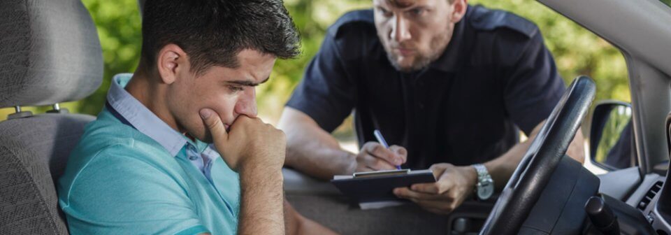 An upset young man receives a traffic ticket from a traffic officer, which will probably have him registered as a high-risk driver.