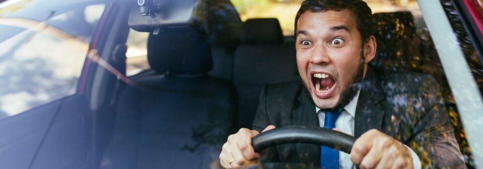 A frustrated male driver behind the wheel screams at something to illustrate how to get the best car insurance as a high-risk driver.