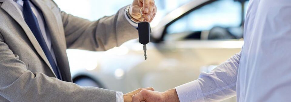 Close up of car salesman giving key to new owner and shaking hands in a used car lot to adorn how to tell if a used car has been in a wreck.