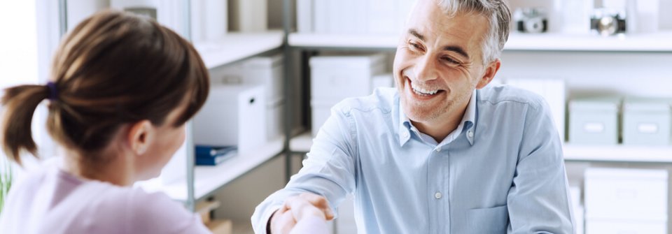 Male insurance agent sitting at desk shaking female customer's hand and depicting what important things to look for in an auto-insurance company.