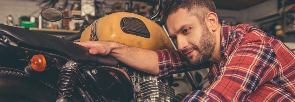 Man cleaning his motorcycle in garage and getting ready to ride. He should take a motorcycle safety course.