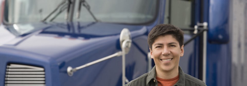 Smiling truck driver standing in front of a semi truck and portraying reasons to buy commercial vehicle insurance.