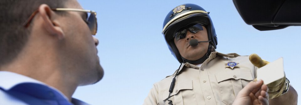 Close up of a man in his car handing license to police officer to illustrate what makes you a high-risk driver.