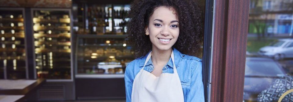 Female business owner standing outside gourmet coffee shop business and portraying when to get commercial insurance for your small business.