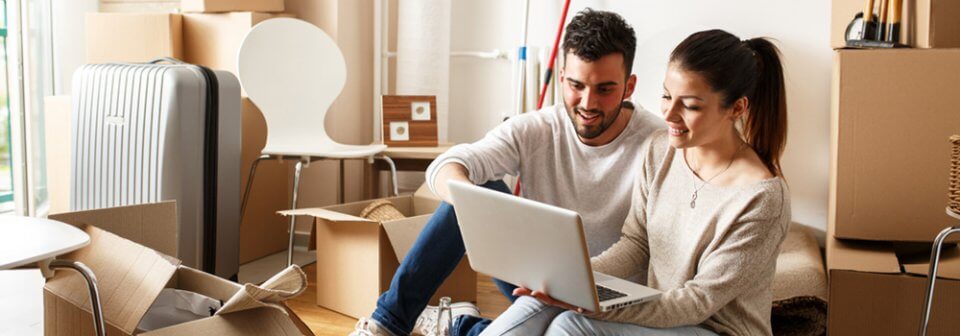 Young couple sitting on the floor of their new apartment and searching for renters insurance online