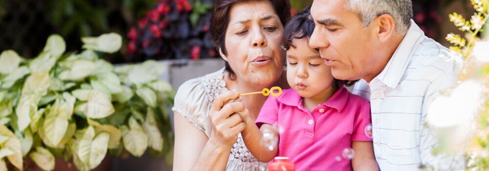 An elderly latino couple blowing bubbles with their grand daughter and portraying the importance of having the right insurance