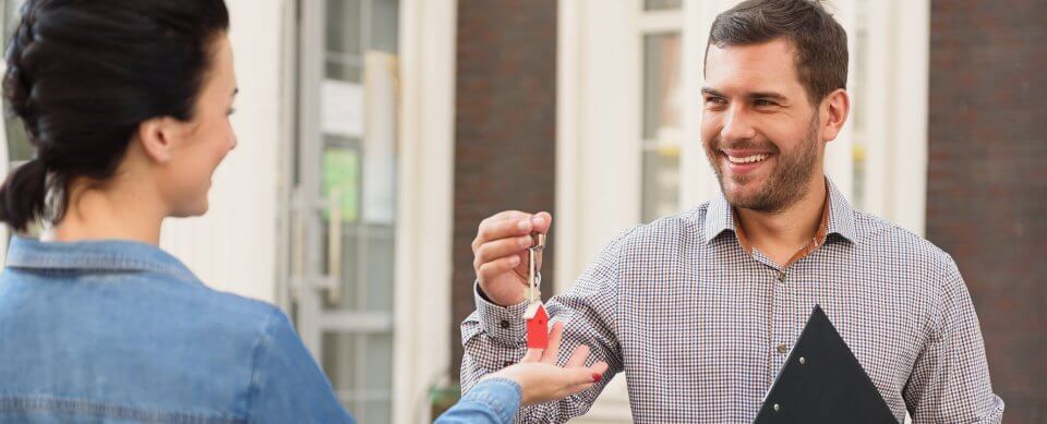 A young landlord handing house keys to a woman. He knows about common landlord mistakes and avoided them.