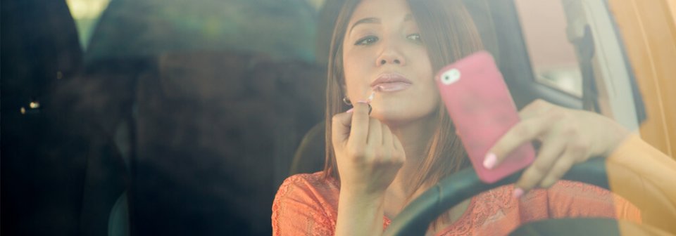 A young latino woman applies makeup while driving and texting, which illustrate some bad driving habits to avoid.