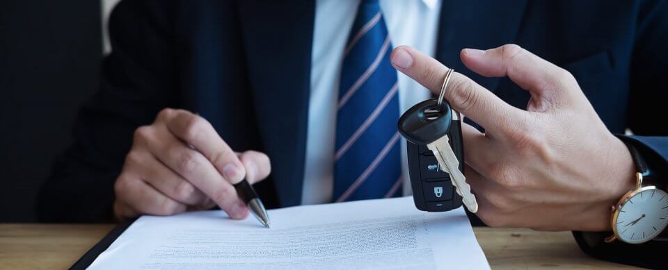 A person signing a rental car agreement that is covered with car insurance.