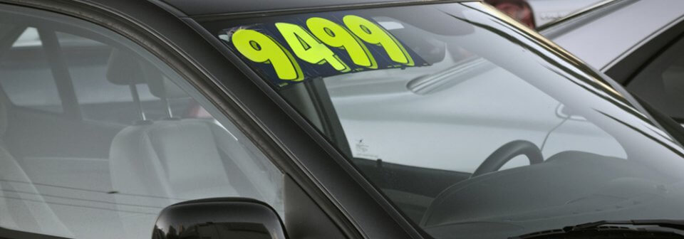 A price tag on a used car in a car lot that illustrates how to buy a used car.