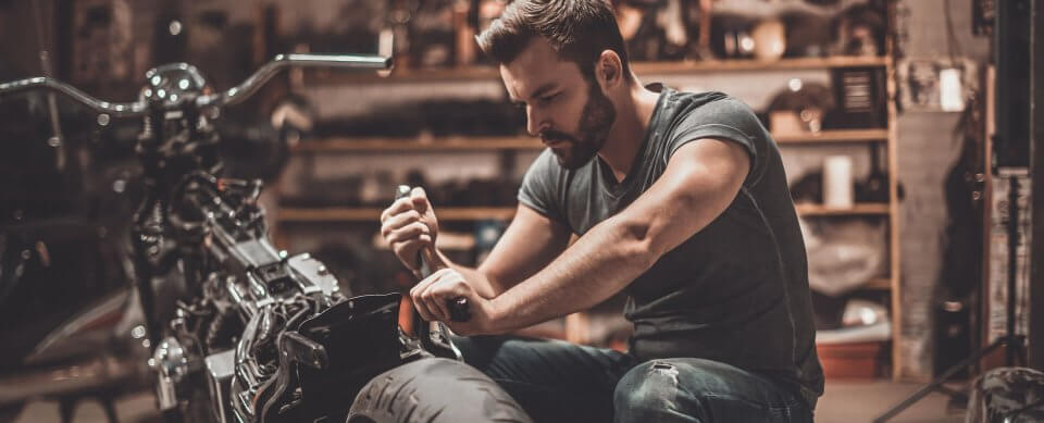 A man putting together his motorcycle in a garage to portray the importance of motorcycle maintenance for safer riding.