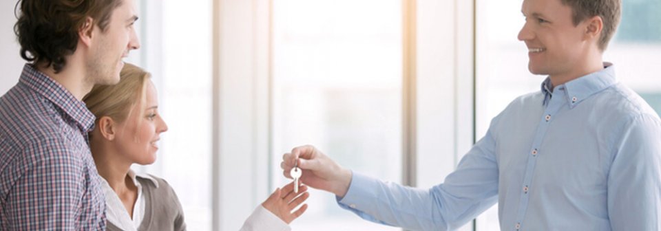 A landlord handing over the keys to an apartment to a young Caucasian couple to illustrate what things renters' insurance does not cover.