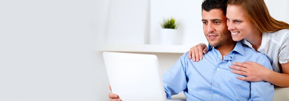 A multi-ethnic couple looking at the computer and smiling as they illustrate tips for getting a better auto-insurance quote online.