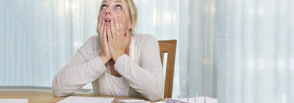 A young, Caucasian woman covering her face in desperation because she suddenly cannot afford health-insurance.