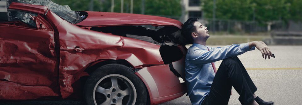 A desperate man sitting in front of his totaled car to illustrate what to do after a hit and run accident.
