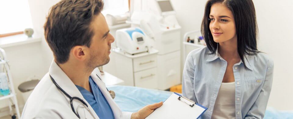 A young, Caucasian woman receiving medical advice from a young Caucasian physician, which is possible thanks to health care coverage.