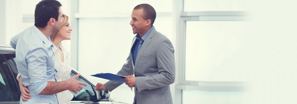 A young Caucasian couple talking with a car sales agent that illustrates 3 ways to beat car dealers at their own games.